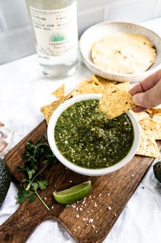 a person dipping guacamole into a bowl with tortilla chips on the side