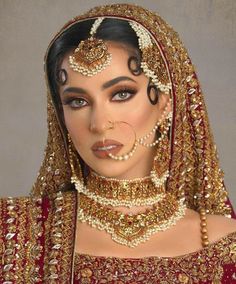 a woman in a red and gold bridal outfit with pearls on her head, nose ring