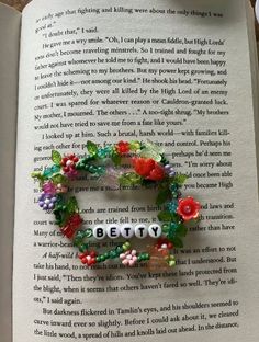 an open book with beads and flowers on the pages that spell out betty's name