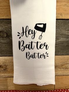 a tea towel with the words hey batter batter on it hanging from a wooden wall