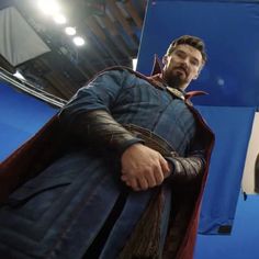 a man dressed as thor stands in front of a blue screen with his hands on his hips