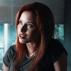 a woman with long red hair wearing a black shirt and silver necklace looking off into the distance