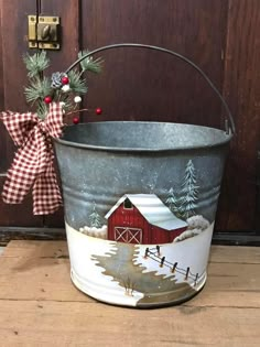 a metal bucket with a christmas scene painted on it and a bow hanging from the handle