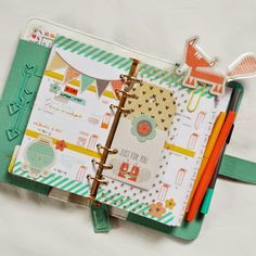 an open planner book sitting on top of a white sheet with markers and pencils