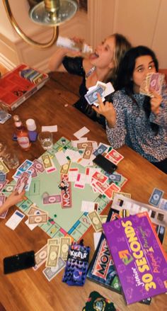 two women sitting at a table with monopoly cards on it and drinks in front of them