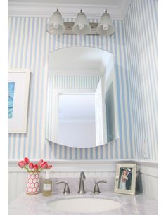 a bathroom with blue and white stripes on the walls, a framed mirror, and a vase with flowers in it