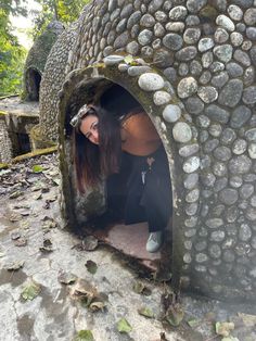 a woman in black pants and white sneakers looking into a stone structure with rocks on it