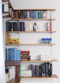 several books are lined up on shelves in a room with white walls and wood flooring