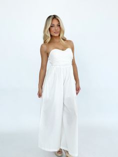 Effortlessly elegant, this versatile jumpsuit is perfect for any summer occasion. The bright and coastal design, featuring a lined and wide leg silhouette, makes it the perfect choice for a wedding, vacation, or resort getaway. The tie detail and strapless design exude luxury and style, while the stretchy smocked back panel ensures both comfort and a flattering fit. With pocket details for added convenience, this jumpsuit is a must-have for your summer wardrobe. Self 100% Cotton Lining 100% Poly Spring Vacation Bandeau Jumpsuits And Rompers, Chic White Strapless Jumpsuit For Summer, Chic White Strapless Jumpsuit For The Beach, Elegant Strapless Jumpsuit For Beach, Summer Party Wide Leg Jumpsuits And Rompers, White Wide Leg Jumpsuits And Rompers For Beach, Summer Vacation Bandeau Jumpsuits And Rompers, Summer Bandeau Jumpsuits And Rompers For Vacation, Bandeau Jumpsuits And Rompers For Summer Vacation