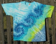 a blue and green tie - dyed t - shirt hanging on a wooden fence post