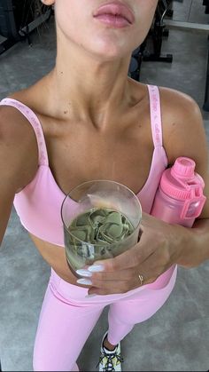 a woman in pink holding a glass filled with water and money while standing next to a gym equipment