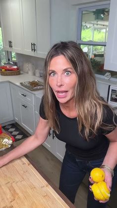 a woman standing in front of a cutting board holding two lemons and looking surprised at the camera