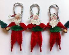 three christmas elves are hanging from the side of a white wall with silver bells attached to them