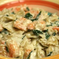 pasta with shrimp and spinach in a creamy sauce on an orange rimmed bowl