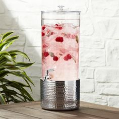 a pitcher filled with ice and raspberries on top of a wooden table next to a potted plant