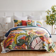 a bed with colorful comforter and pillows on top of it in a white room