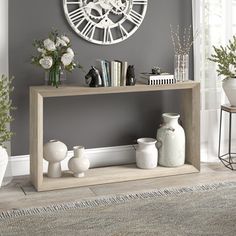 a clock on the wall above a shelf with vases and flowers in front of it