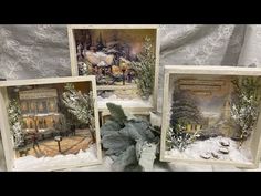 four framed christmas cards are sitting on a white cloth covered tablecloth, with snow and trees in the background