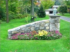 a stone wall and flower bed in the middle of a yard with trees around it