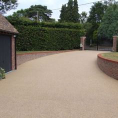 a driveway with a brick wall and gate in the center, surrounded by hedges on both sides