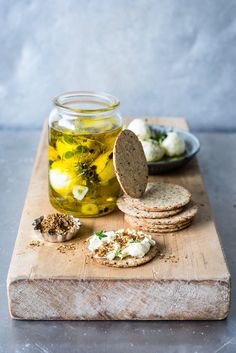 a wooden cutting board topped with crackers and olives next to a jar of olive oil