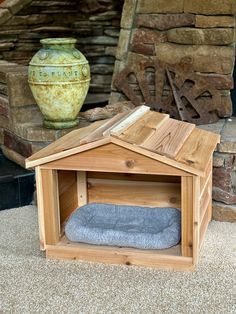 a dog house made out of wood with a blue blanket in the corner and a vase behind it