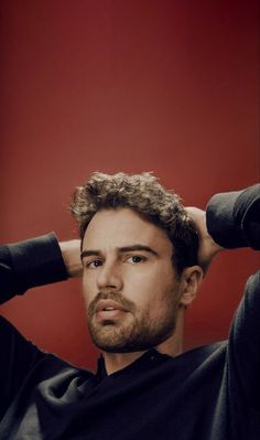 a man with curly hair is holding his hands behind his head and looking off to the side