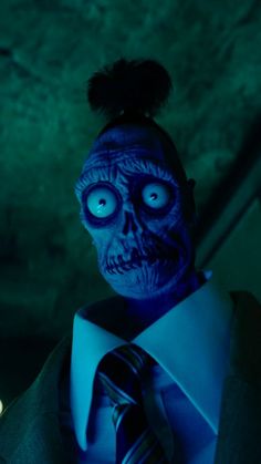 a man in a suit and tie with blue light on his face is staring at the camera