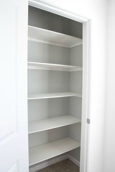 an empty closet with white shelves and carpeted flooring in front of the door