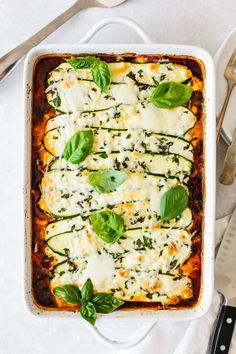 a casserole dish with spinach, cheese and sauce in it next to utensils