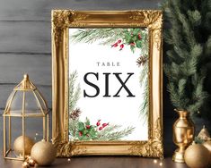 a table sign sitting on top of a wooden table next to gold ornaments and a christmas tree