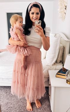 a woman taking a selfie while holding a baby in her arms and wearing a pink tulle skirt