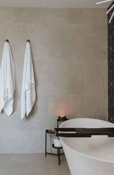 two white towels hanging on the wall next to a bathtub with candles in it