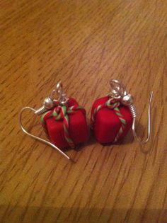 two red wrapped gift boxes with green bows on them sitting on a wooden table next to silver earwires