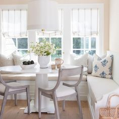 a white table and chairs in front of two windows with pillows on the couches