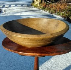 an old wooden bowl sitting on top of a table next to a sidewalk with snow