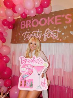 a woman holding a sign in front of balloons and streamers with the words brooke's twenty best written on it