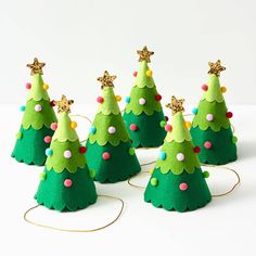 small felt christmas trees are lined up on a white surface with gold decorations around them