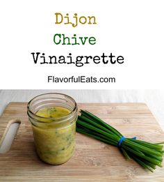 a jar filled with yellow liquid sitting on top of a wooden cutting board next to green onions