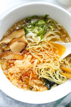 a white bowl filled with noodles, meat and veggies next to chopsticks