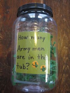 a jar filled with gummy bears sitting on top of a wooden table next to a sign that says how many army men are in the tub?