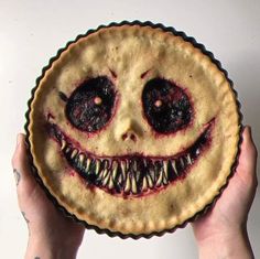 a person holding up a pie with an evil face on it