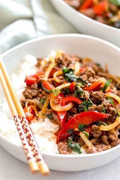 a white bowl filled with meat and vegetables next to chopsticks on top of rice