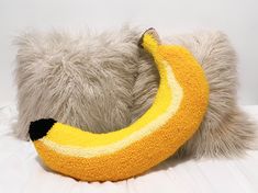 a stuffed banana sitting on top of a white bed next to a gray and yellow pillow