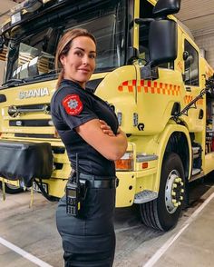 a woman police officer standing in front of a yellow fire truck with her arms crossed