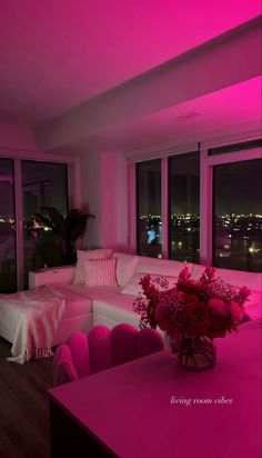 a living room filled with furniture and pink lighting on the walls, windows overlooking city lights