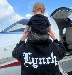 a man holding a child in front of an airplane with the door open to another plane