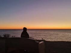 a man sitting on top of a bench near the ocean at sunset or sunrise time