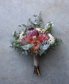 a bridal bouquet with red and white flowers, greenery and berries sits on a concrete surface