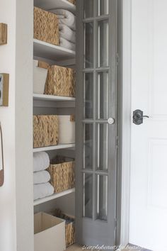 an open closet with baskets and towels on the shelves in front of it, next to a door